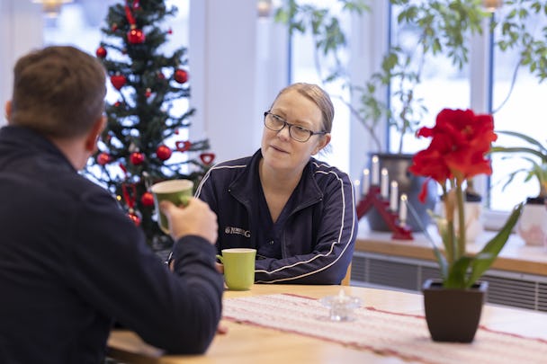 Rehabassistenten Maja Lukkaroinen i Norberg pratar med en man vid ett bord med en julgran i bakgrunden.