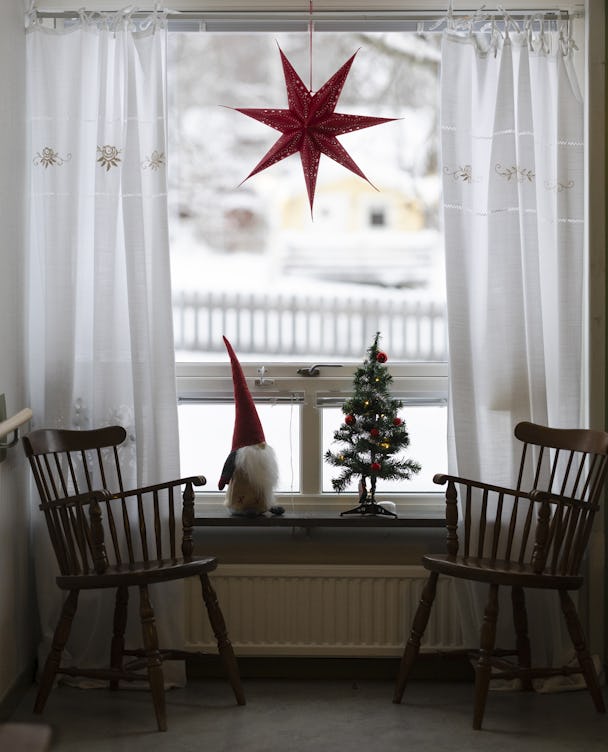 Ett fönster med två tomma trästolar och en julgran.