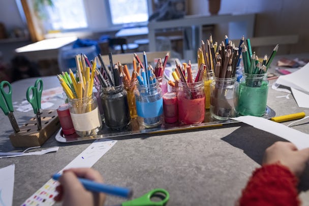 En flicka gör konst med färgpennor på ett bord.