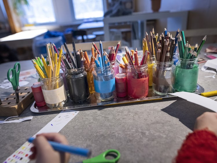 En flicka gör konst med färgpennor på ett bord.