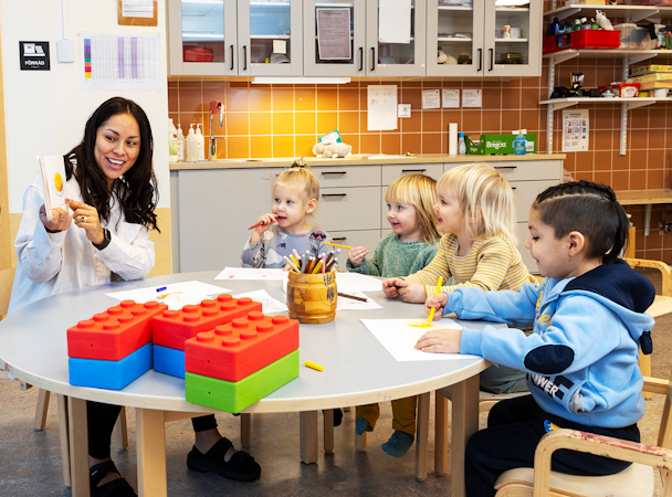 Specialistbarnskötare Daglem Nilsson på Munktellstadens förskola i Eskilstuna visar en bok för en grupp barn som sitter runt ett bord.