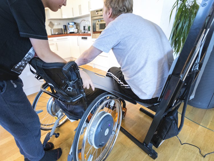 En person som hjälper en man ta sig till sin rullstol.
