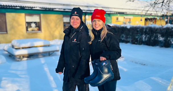 Sofia Gunnarsson, barnskötare och ombud för fackförbundet Kommunal och Linda Ahlgren, huvudskyddsombud fackförbundet Kommunal, som står i snön framför ett hus och håller upp ett par skor.
