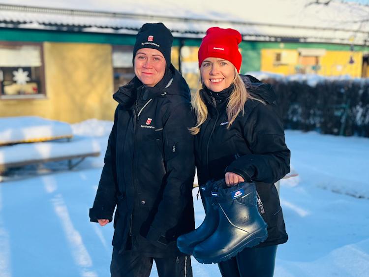 Sofia Gunnarsson, barnskötare och ombud för fackförbundet Kommunal och Linda Ahlgren, huvudskyddsombud fackförbundet Kommunal, som står i snön framför ett hus och håller upp ett par skor.