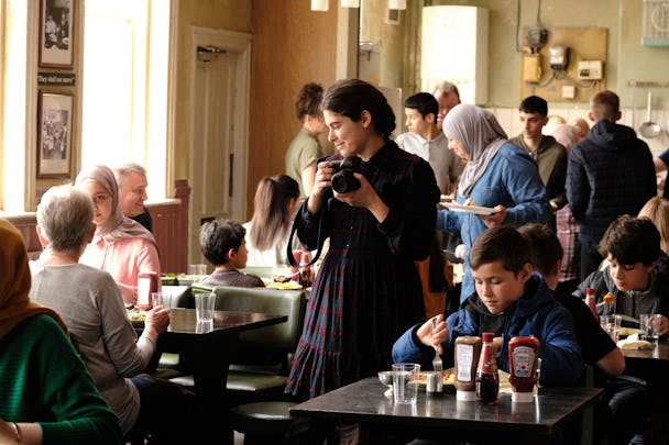 En grupp människor som sitter vid bord på en restaurang. Scen ur filmen The Old Oak.