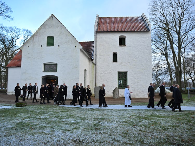 Ett begravningståg som lämnar en vit kyrka en frostig dag.