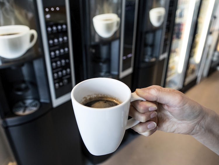 En person håller en kopp kaffe framför en kaffeautomat.