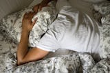 En man ligger utslagen i en säng med en kudde över huvudet