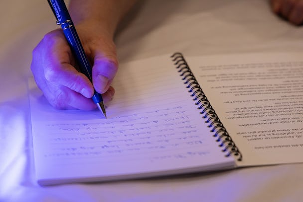 En person som skriver i en dagbok med en penna, med tryckt text på sidan till vänster.