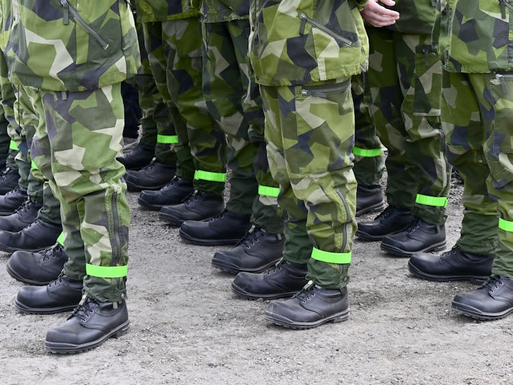 En grupp soldater i kamouflageuniformer med gröna reflexband runt benen som står i formation.