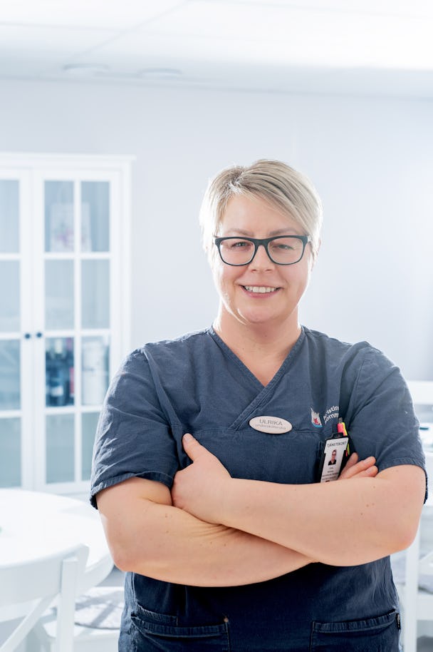 Undersköterskan Ulrika Beckman i scrubs stående med armarna i kors i en klinisk miljö.