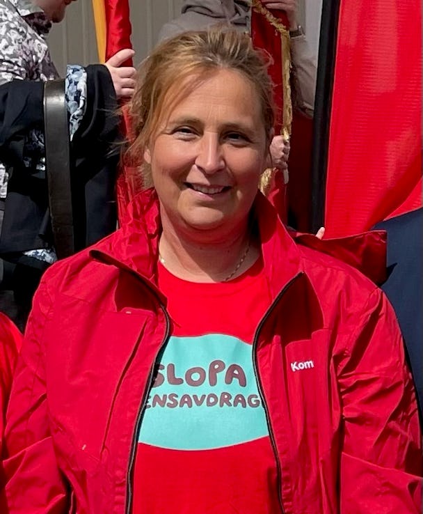 Kvinna i en röd jacka och t-shirt ler mot kameran.