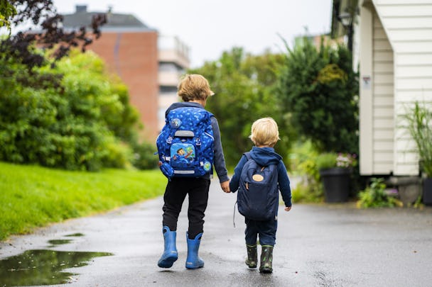Två barn med ryggsäckar som går hand i hand på en våt stig.