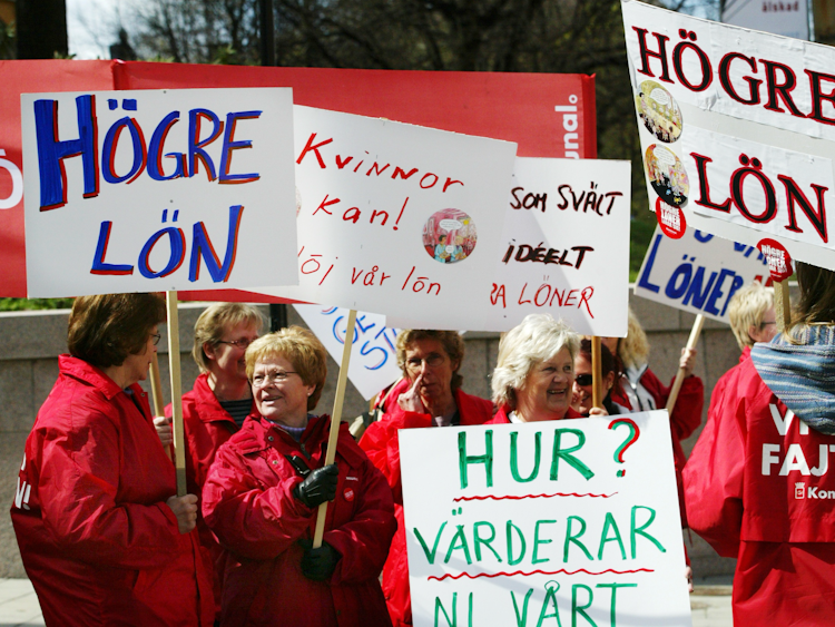 Demonstranter i röda jackor håller skyltar som förespråkar högre löner och jämställdhet i löner.