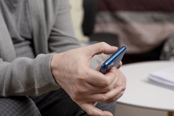 Detailvy av en äldre persons händer som använder en smartphone i en hemmiljö.