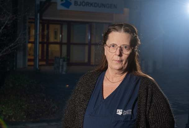 En medelålders kvinna med glasögon i blus och kofta står framför en byggnad märkt "Björkdungen".