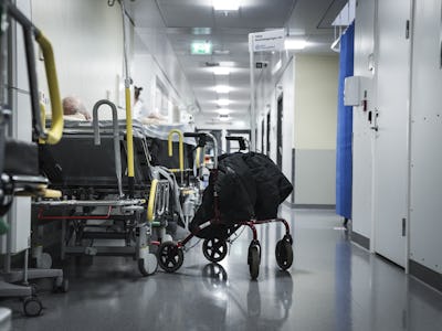 Bild på en sjukhuskorridor med patienter som sitter i rullstolar och sjukhussängar längs med väggarna, inklusive klinisk skyltning och stängda dörrar.