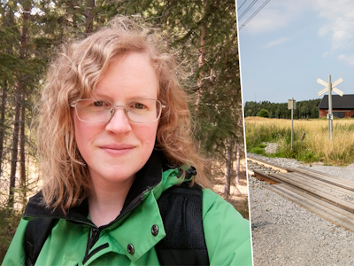En lockig kvinna med glasögon i grön kavaj. En grusväg leder mot en lada, skylt som visar en järnvägsövergång i närheten.