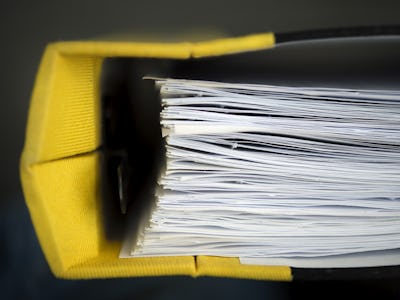 En inzoomad vy av en stor mängd dokument staplade i en gul pärm.