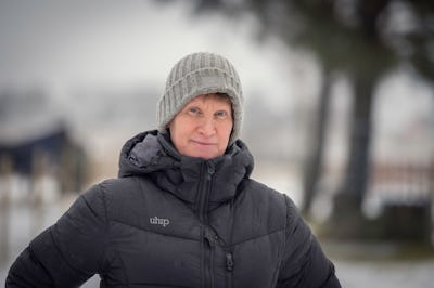Nina Lundberg i grå mössa och svart jacka står utomhus på en snöig dag med något suddigt trädlandskap i bakgrunden.