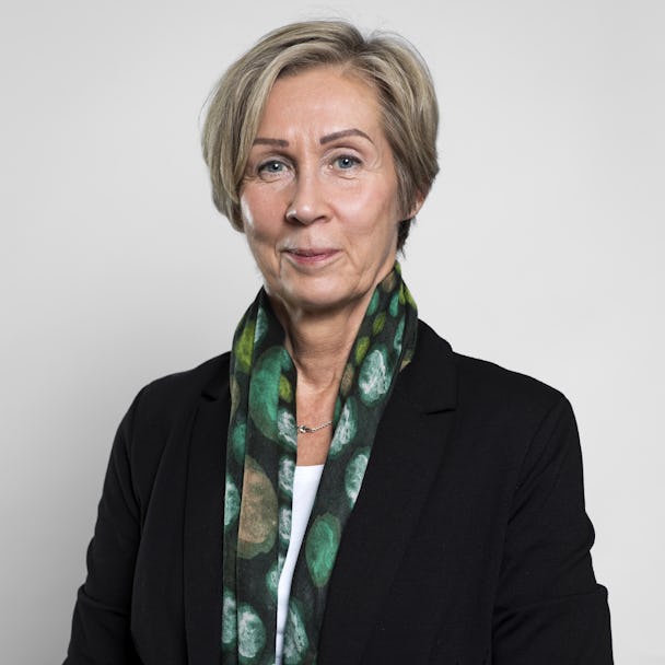 Annett Olofsson, förbundsjurist på LO TCO Rättsskydd, med kort, ljusblont hår har på sig en svart kavaj och en grön mönstrad scarf och poserar mot en vit bakgrund.