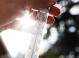 Närbild av en hand som håller i en termometer med en blå linje som visar temperaturavläsningen, solstrålar syns i bakgrunden.