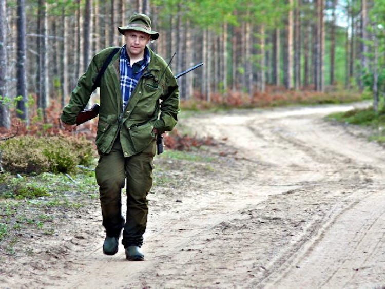 En man kommer och går längs en skogsväg, klädd för jakt.