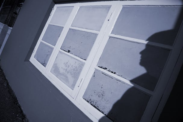 En skugga av en person mot en husvägg med ett stort fönster.