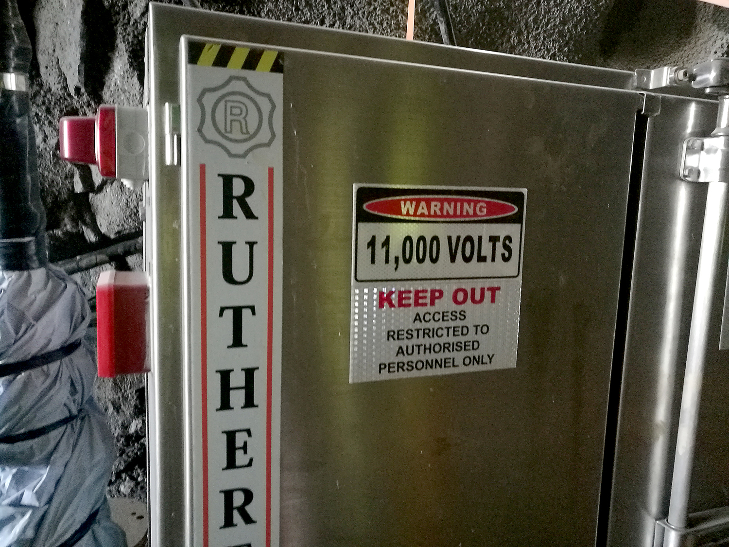 Bilden föreställer ett grått metallskåp med en varningsskylt på. Warning, 11000 volts, keep out, access restricted tp authorised personnel only, står det på skylten.