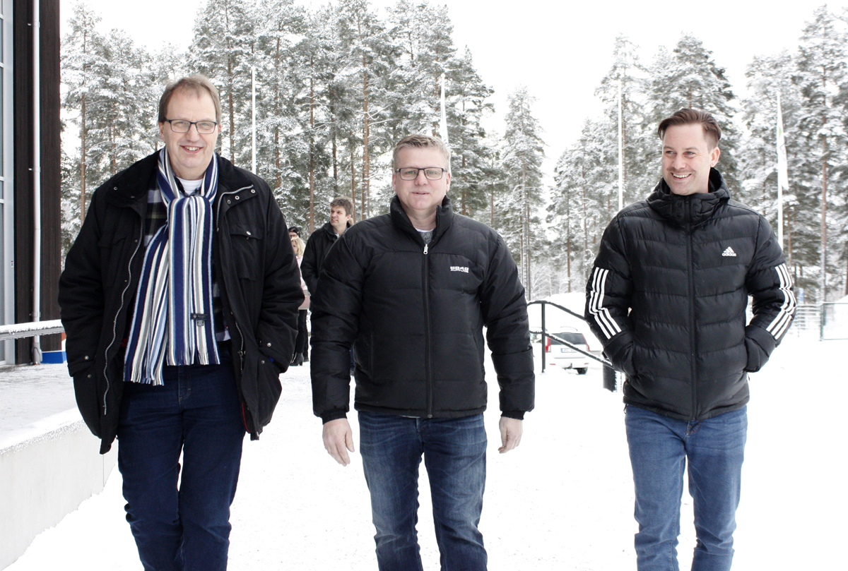Bilden föreställer tre leende män som går mot kameran i en snötäckt omgivning.