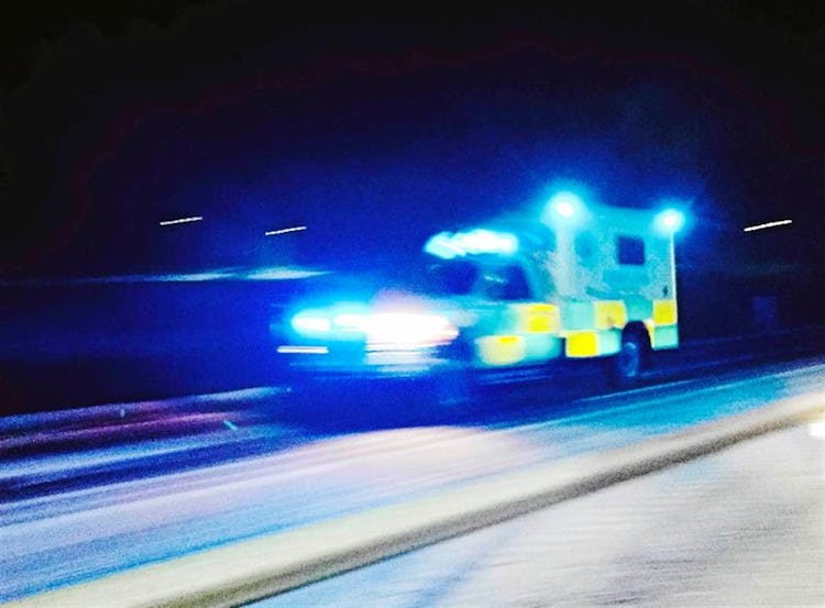 En ambulans med sirener åker på en mörk landsväg