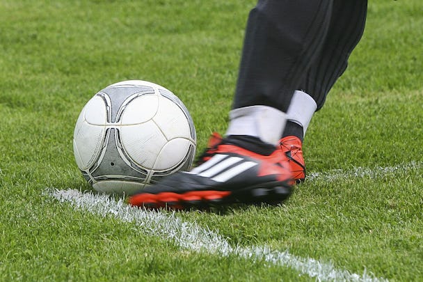 En fot i röd sko sparkar mot en fotboll på en gräsplan.