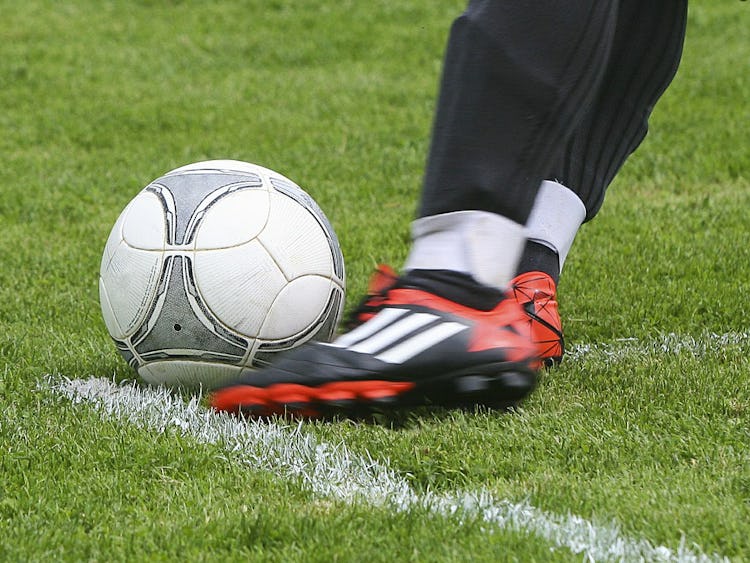 En fot i röd sko sparkar mot en fotboll på en gräsplan.