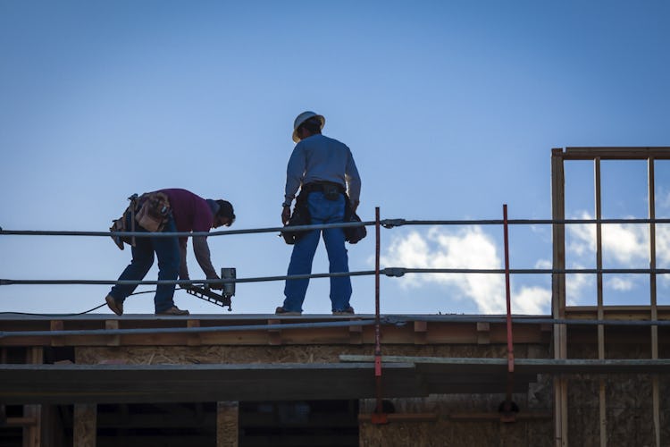 Två byggarbetare på hög höjd mot en blå himmel.
