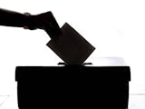 Silhuetten av en hand som lägger en röstsedel i en valurna