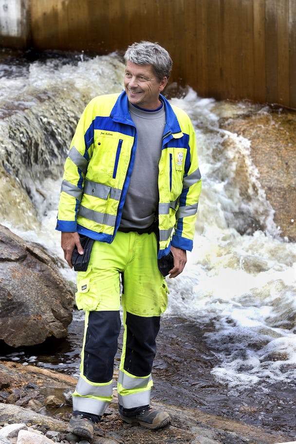 En person i gula reflexkläder står framför ett fall i ett forsande vattendrag.