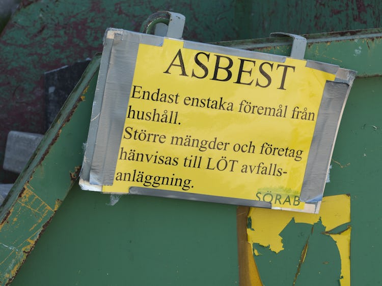 En grön container med en skylt där det står: "Asbest. Enstaka föremål från hushåll. Större mängder och företag hänvisas till LÖT avfalls-anläggning. Sörab."