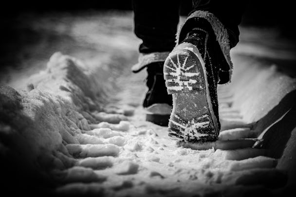 Närbild på ett par fötter klädda i kängor som går i ett traktorspår i snön.