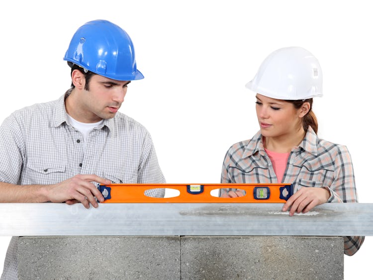 En man och en kvinna i bygghjälmar samarbetar för att jämna ut ett vattenpass.