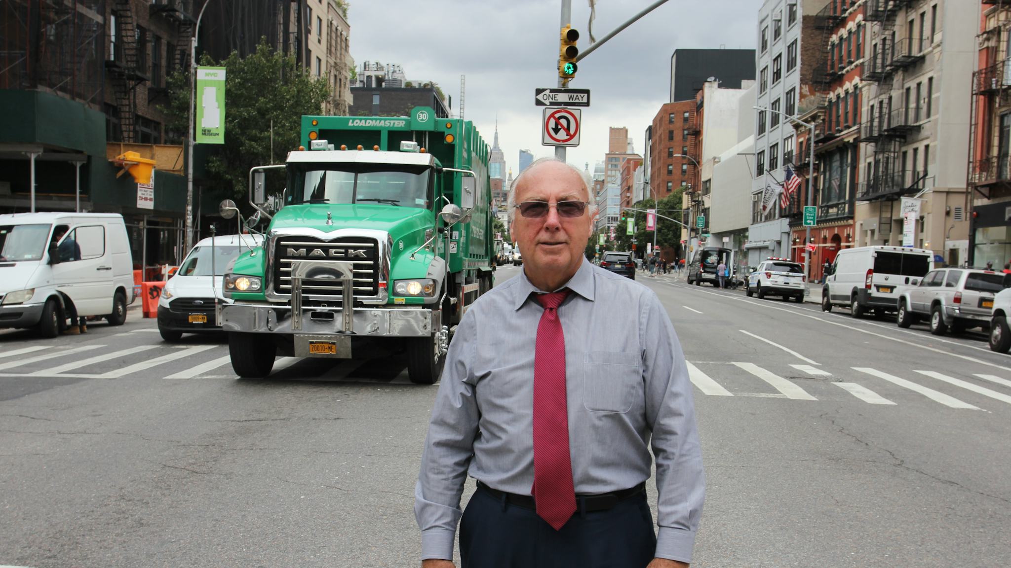 Chris Erikson står på ett övergångsställe med en stadsvy i bakgrunden, bland annat fronten på en stor grön lastbil.