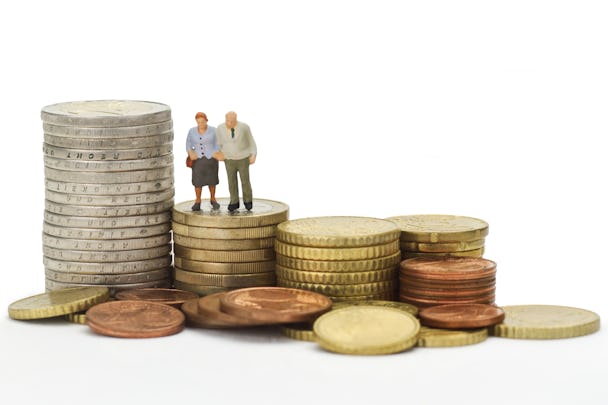 Leksaksfigurer av ett äldre par som står på en trave mynt, bland flera sådana travar.