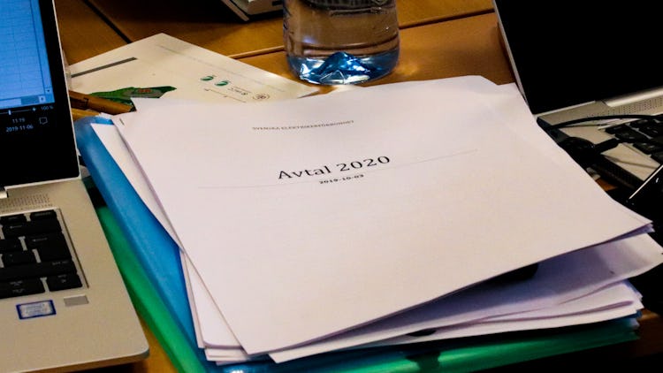 En bunt papper på ett mötesbord, med texten Avtal 2020 på omslaget