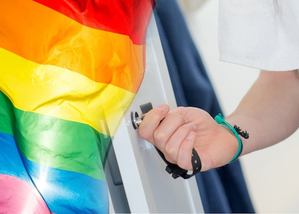 Handen på en person som låter upp ett skåp i ett omklädningsrum, noterat invid en prideflagga