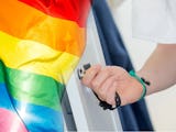 Handen på en person som låter upp ett skåp i ett omklädningsrum, noterat invid en prideflagga