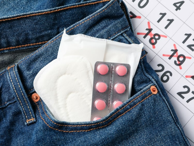 Ett par jeans med mensbindor och p-piller i fickan, framför en kalender med överkryssade datum.
