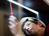 En ung person i skyddshjälm mäter spänning med ett verktyg