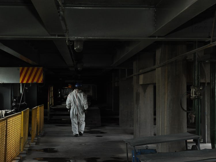 En arbetare i vit skyddsoverall går genom en källare