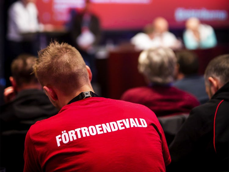 Ryggtavlan på en person på ett möte. Personens tröja är röd och har ordet "Förtroendevald" tryckt i vita bokstäver.