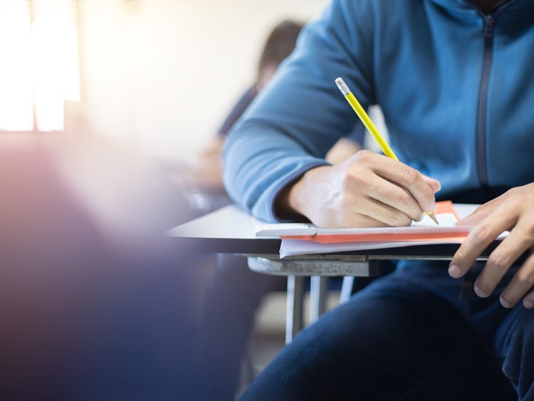 En person sitter vid en skolbänk och skriver på ett papper