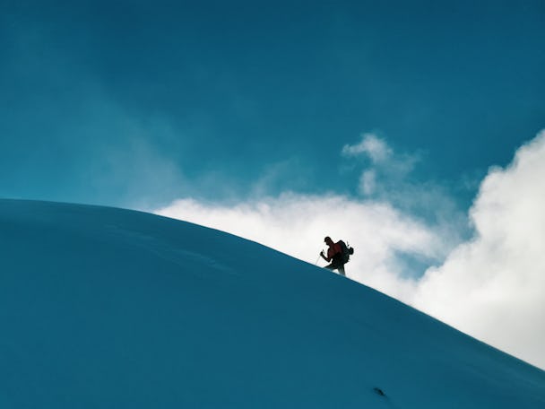Silhuetten av en person som bestiger ett snöigt berg